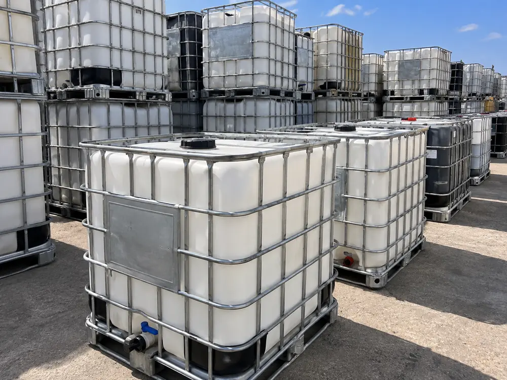 Clear-bottled food-grade IBC totes stacked and graded in the yard